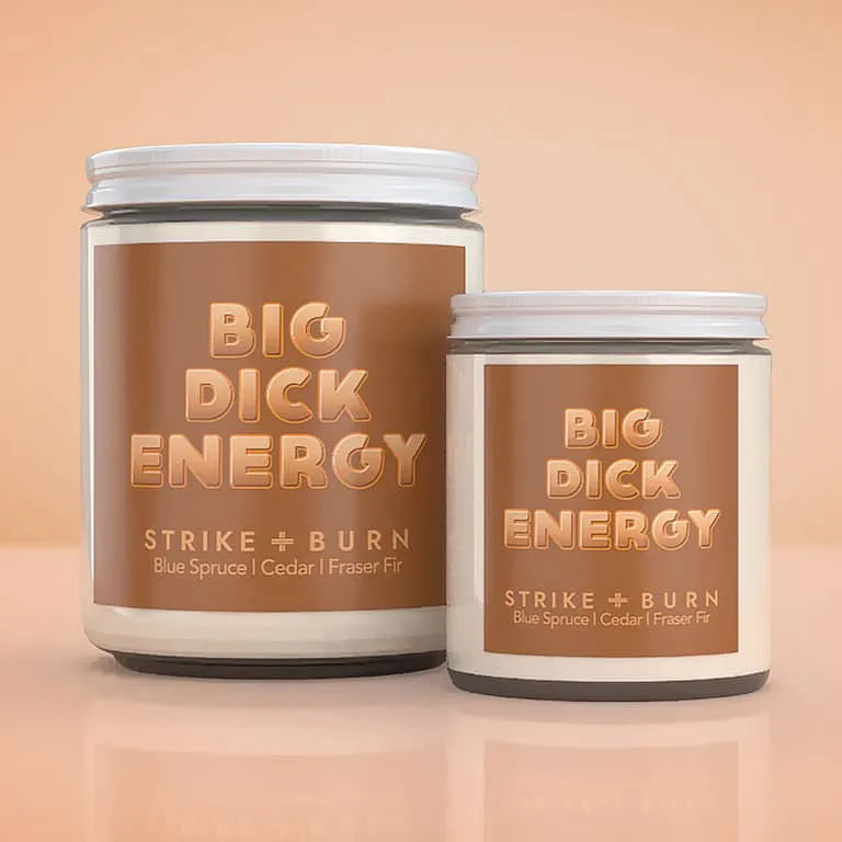 Two cylindrical jars of 'Big Dick Energy' Strike + Burn wax melts on a warm peach background. The larger jar is white with a brown label, and the smaller jar is cream with a matching brown label, both featuring metallic gold text.